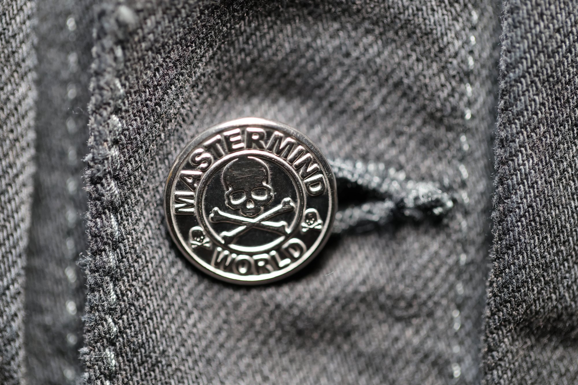 Macro of the engraved metal shank button against washed grey denim.
